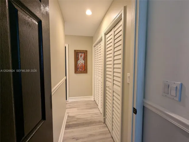 L-shaped and well-lit hallway, featuring wood-style flooring, neutral walls, and organized linen closet space, and air handler closet, creating a neat transition between rooms.