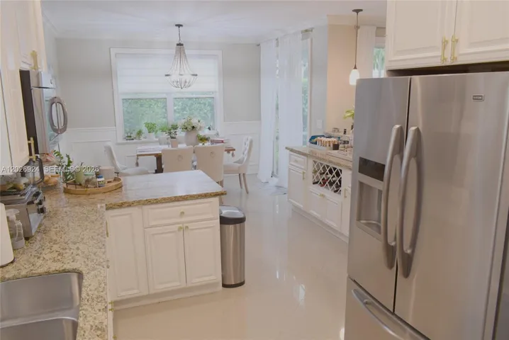 Bright kitchen and dining space featuring granite countertops, white cabinetry, stainless-steel appliances, and a well-lit eating area with large windows and elegant seating.