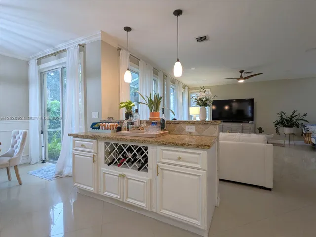 Central bar-style island with granite countertop, pendant lighting, and built-in storage, serving as an elegant divider between the kitchen and the open living area.