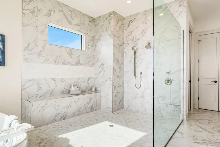 Meticulously designed walk-in shower showcasing an elongated stone bench and custom glass enclosure.