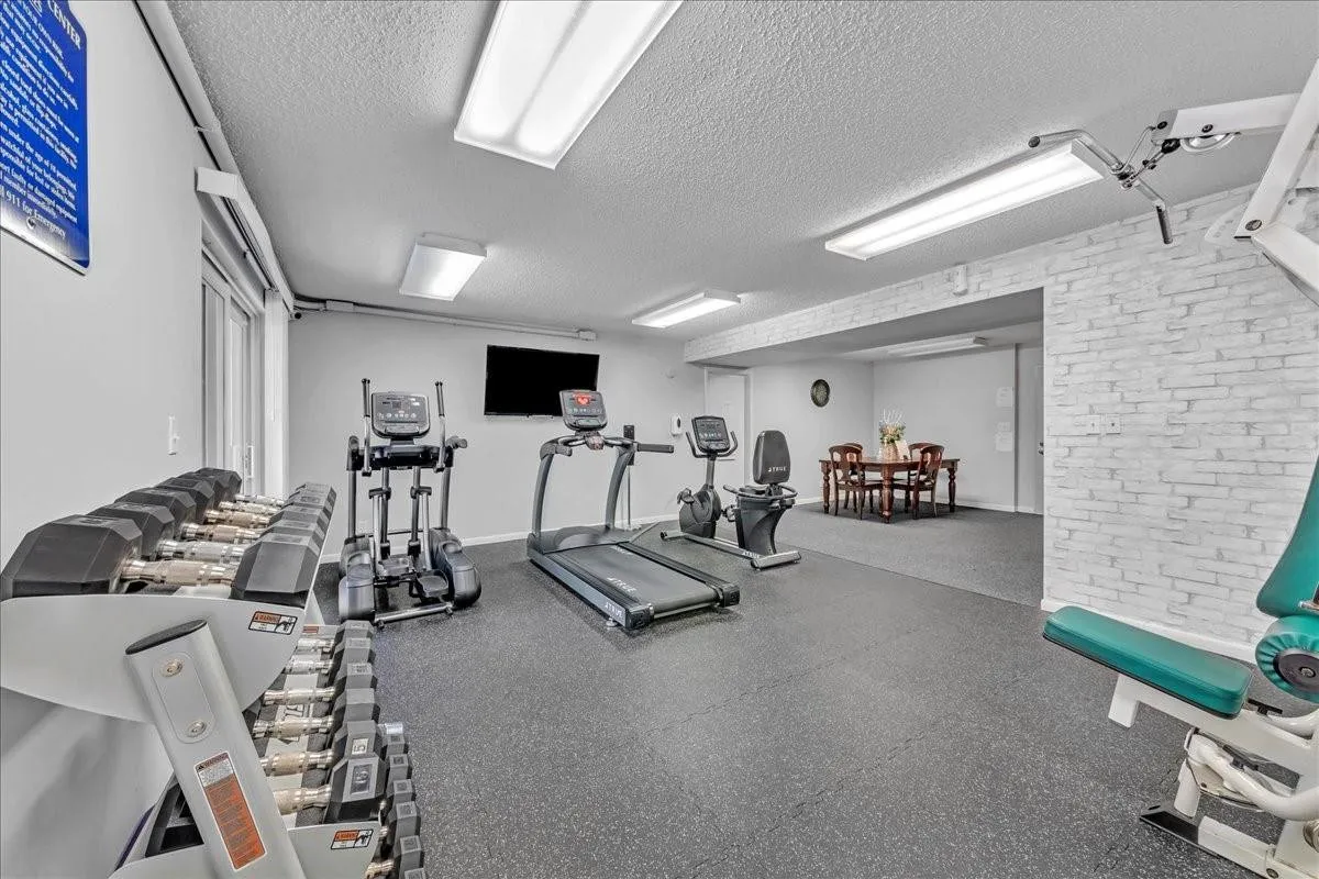 Condo fitness room with treadmills, free weights, and pool view — ideal for active coastal living.