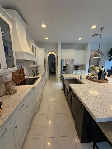 VIEW OF STAINLESS STEEL FARMHOUSE SINK, ELECTRIC STOVE TOP, AND CUSTOM HOOD WITH DOUBLE GLASS DOORS ON EACH SIDE. ARCHED ENTRYWAY LEADING TO MAIN DINING ROOM.