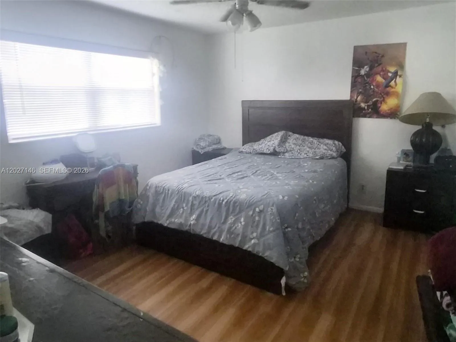 Generous primary bedroom featuring warm laminate wood flooring, a wide window bringing in natural light, and plenty of space for a full king