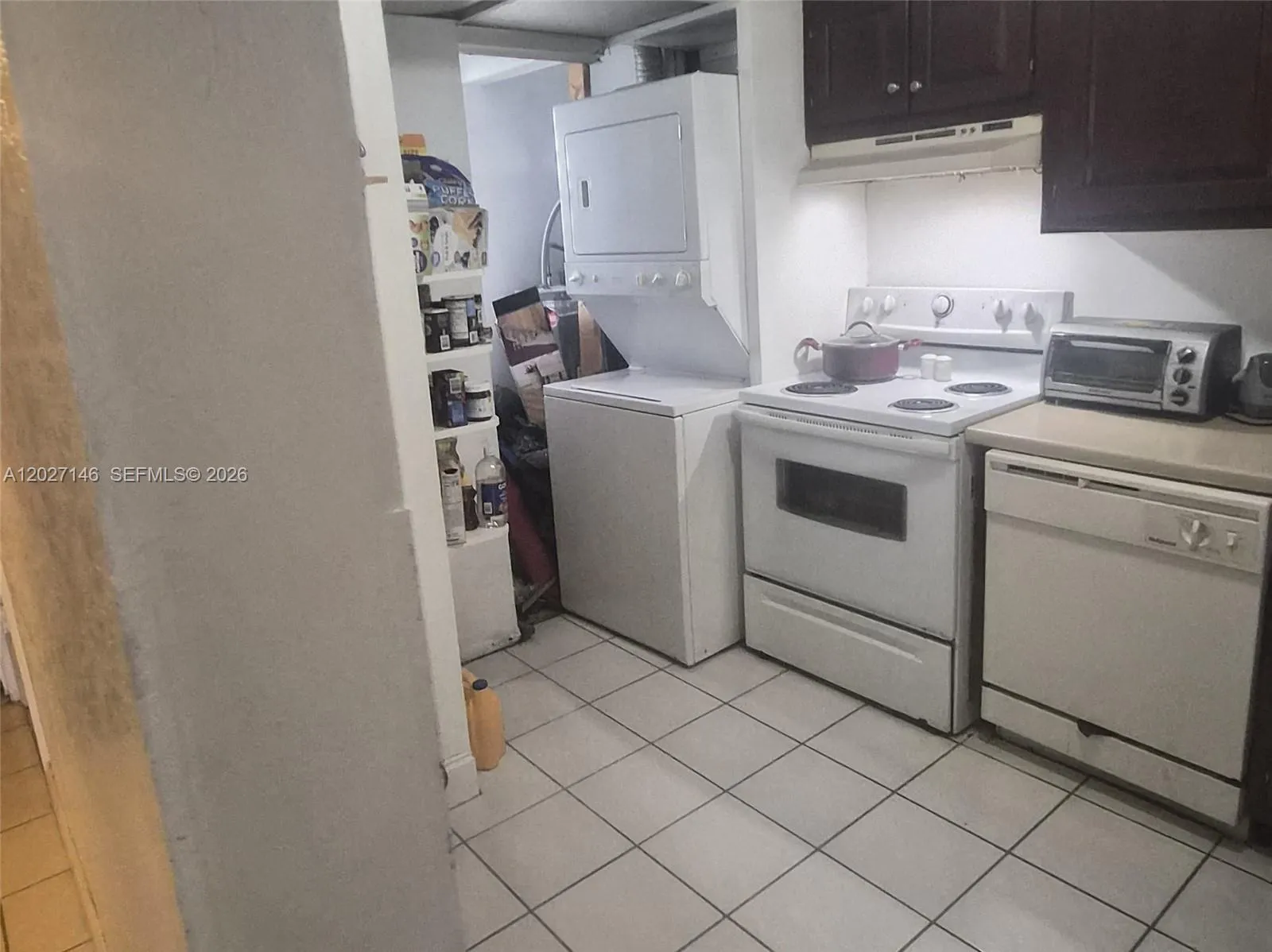 Efficient galley kitchen with cabinetry, ample counter space for meal prep, matching appliances, washer/dryer, clean tile flooring, and a bright central lighting strip.