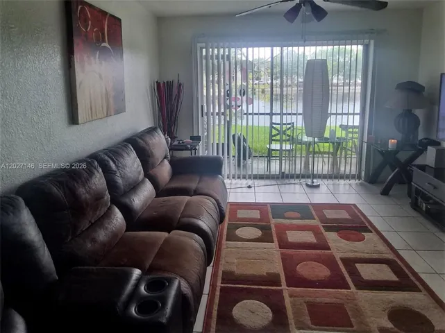 Light-filled, spacious living area featuring a large neutral tile layout, a comfortable sectional sofa setup, and massive sliding glass doors leading out to the patio.