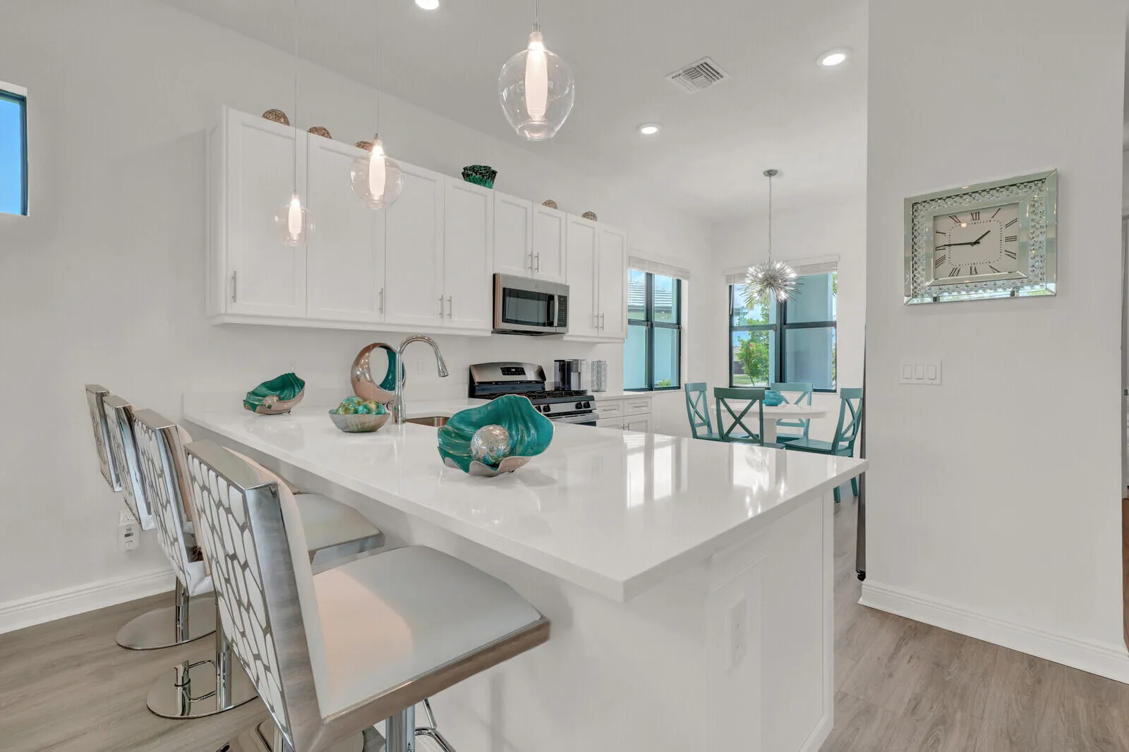 Kitchen featuring a white countertop island with integrated sink, white cabinetry, stainless steel appliances, and pendant lighting