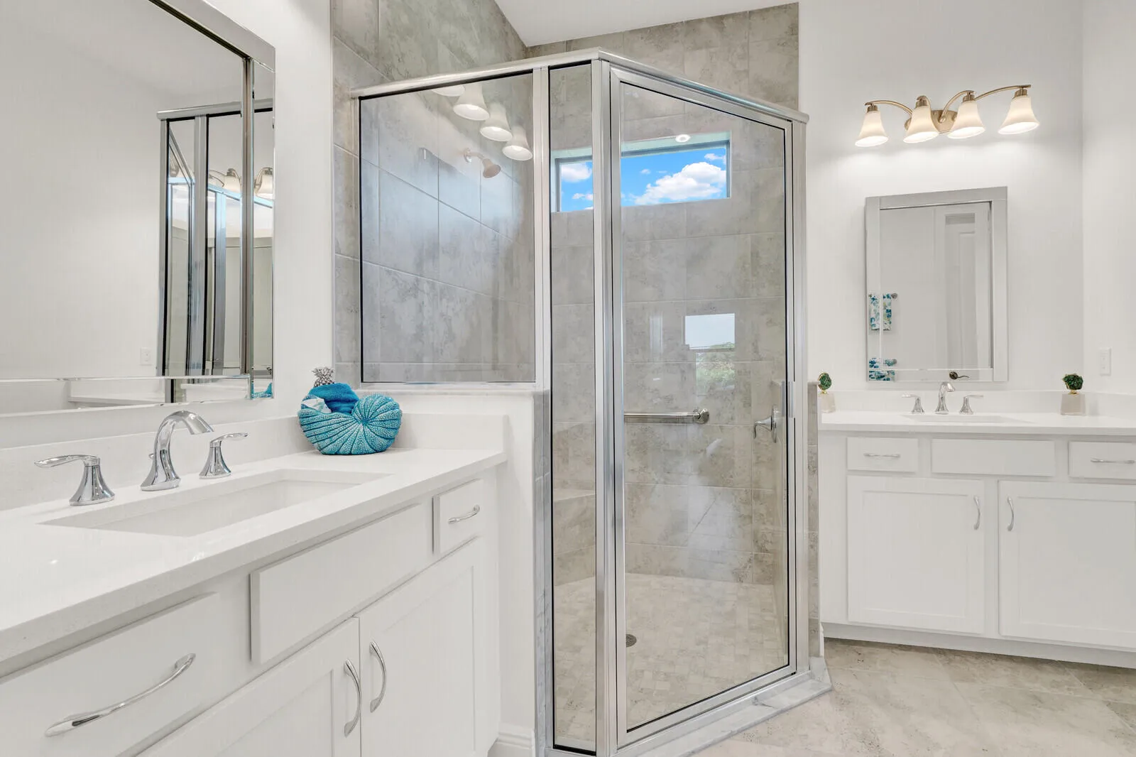 Spacious bathroom featuring a glass-enclosed shower with a transom window, dual white vanities with undermount sinks, and chrome fixtures