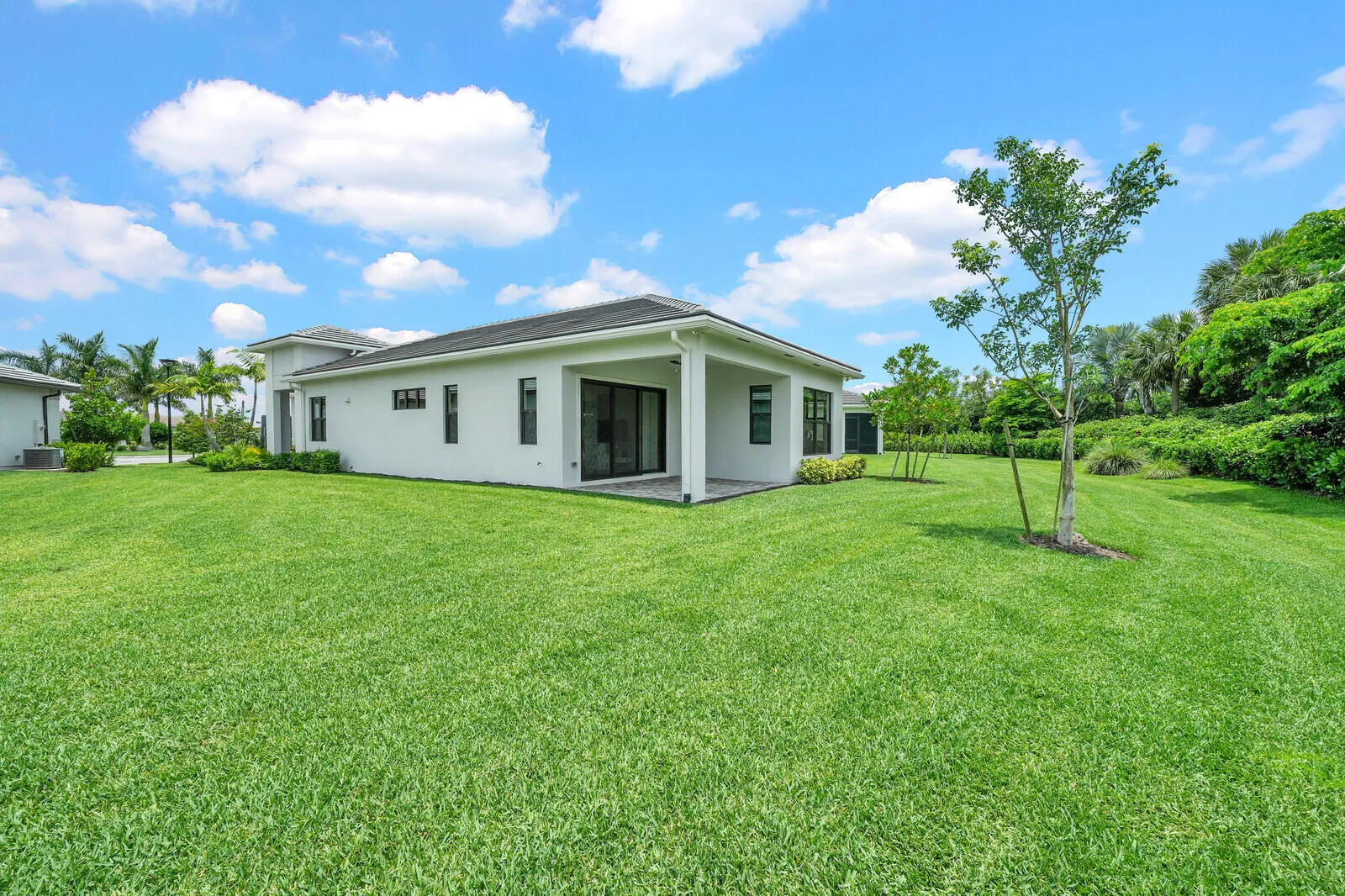 Expansive green lawn surrounds a modern stucco exterior with a covered patio