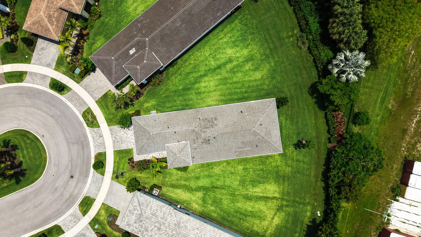 Residential property featuring a light-colored shingle roof, surrounded by expansive green lawns