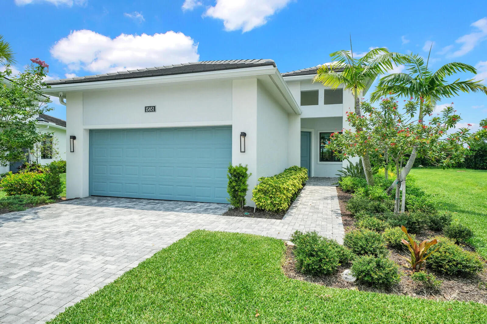 Contemporary exterior featuring a two-car garage with a blue door, a paver driveway, an inviting paver walkway, lush landscaping, and a well-manicured lawn