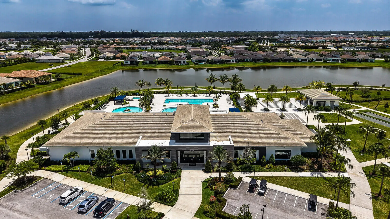 Community amenity building with multiple swimming pools, extensive patio space, and surrounding palm trees