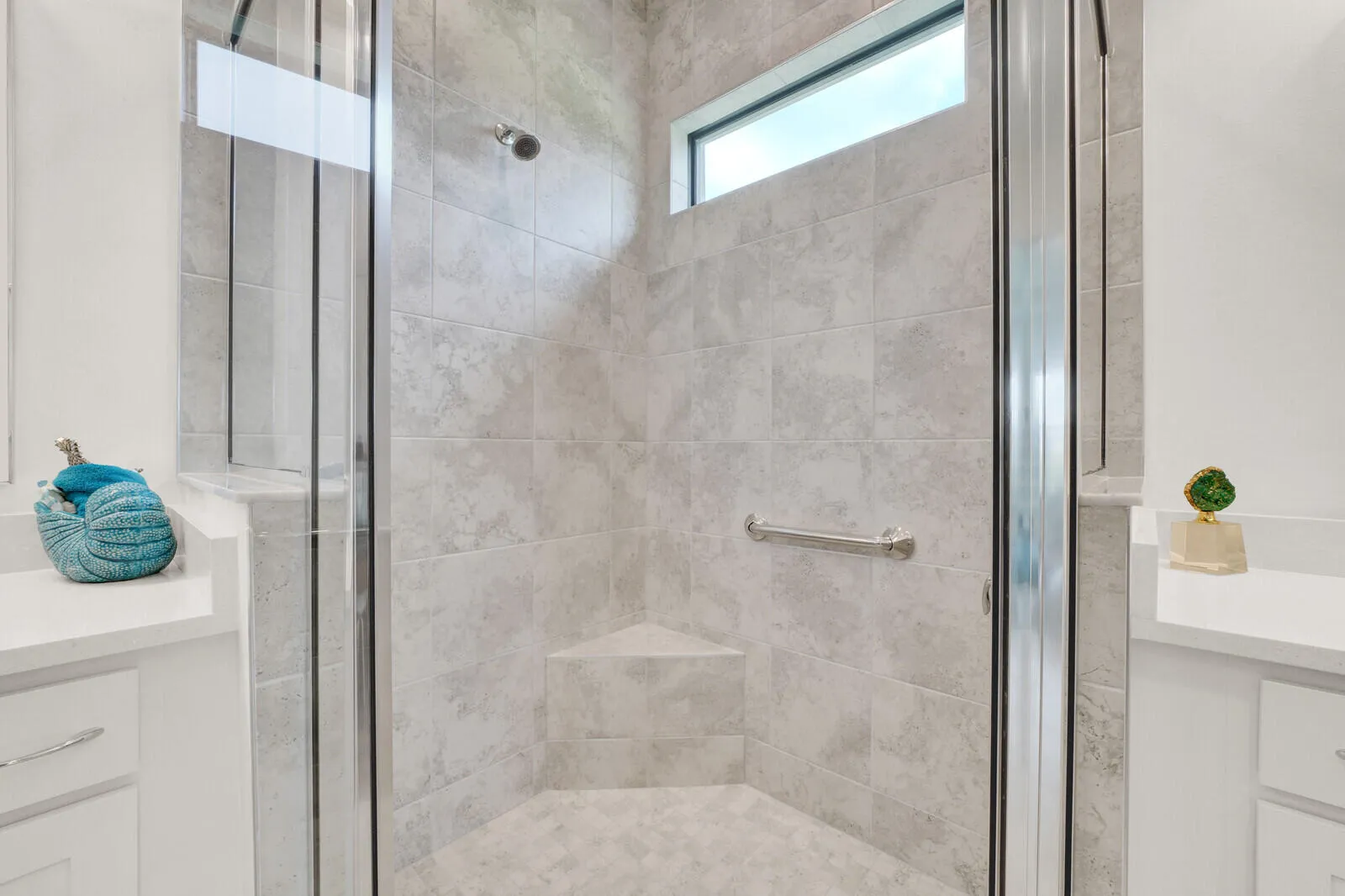 Glass-enclosed shower featuring gray large-format tile, corner bench seating, a fixed shower head, and a transom window