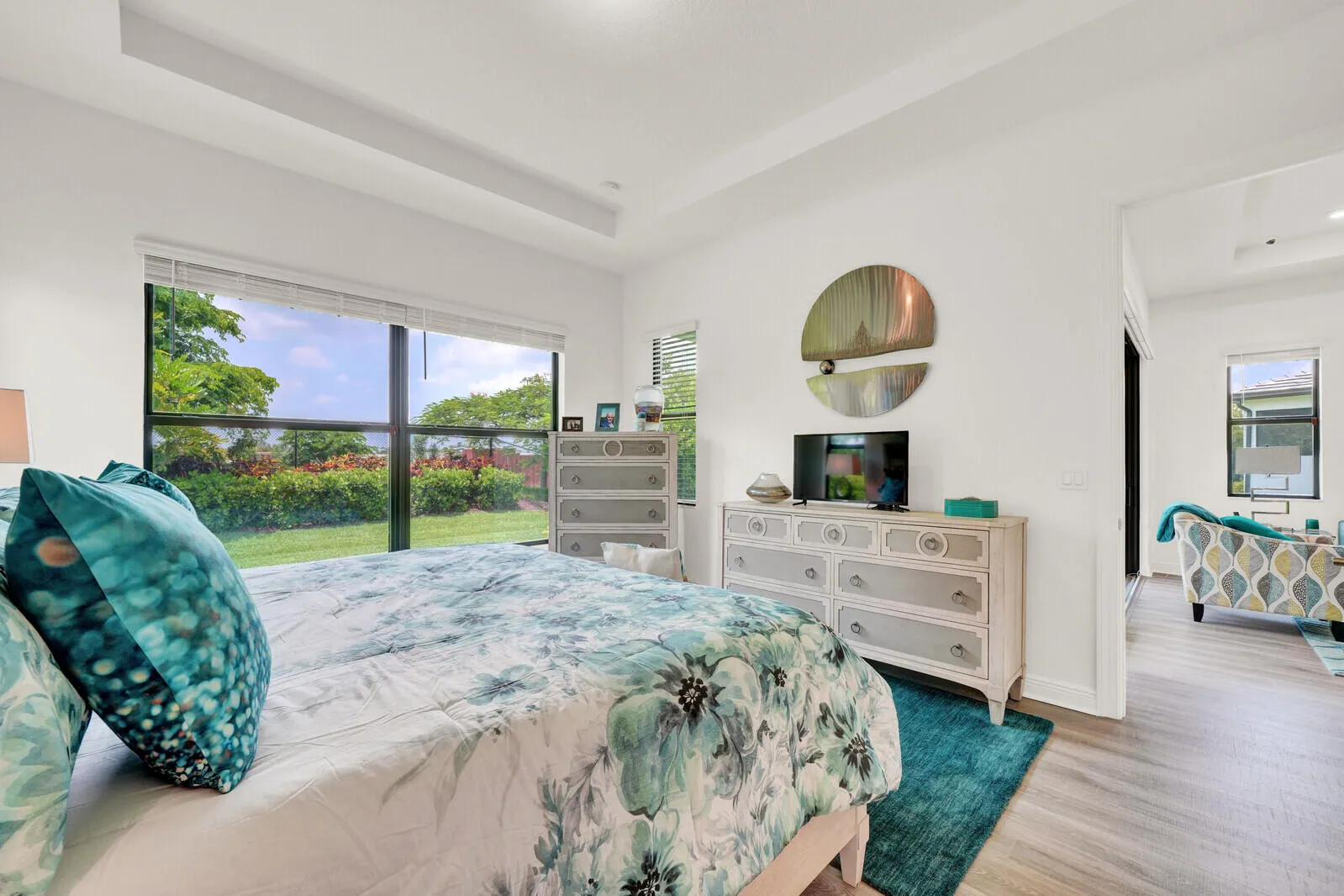 Spacious bedroom with a large window overlooking a manicured lawn, tray ceiling, and wood-finish flooring