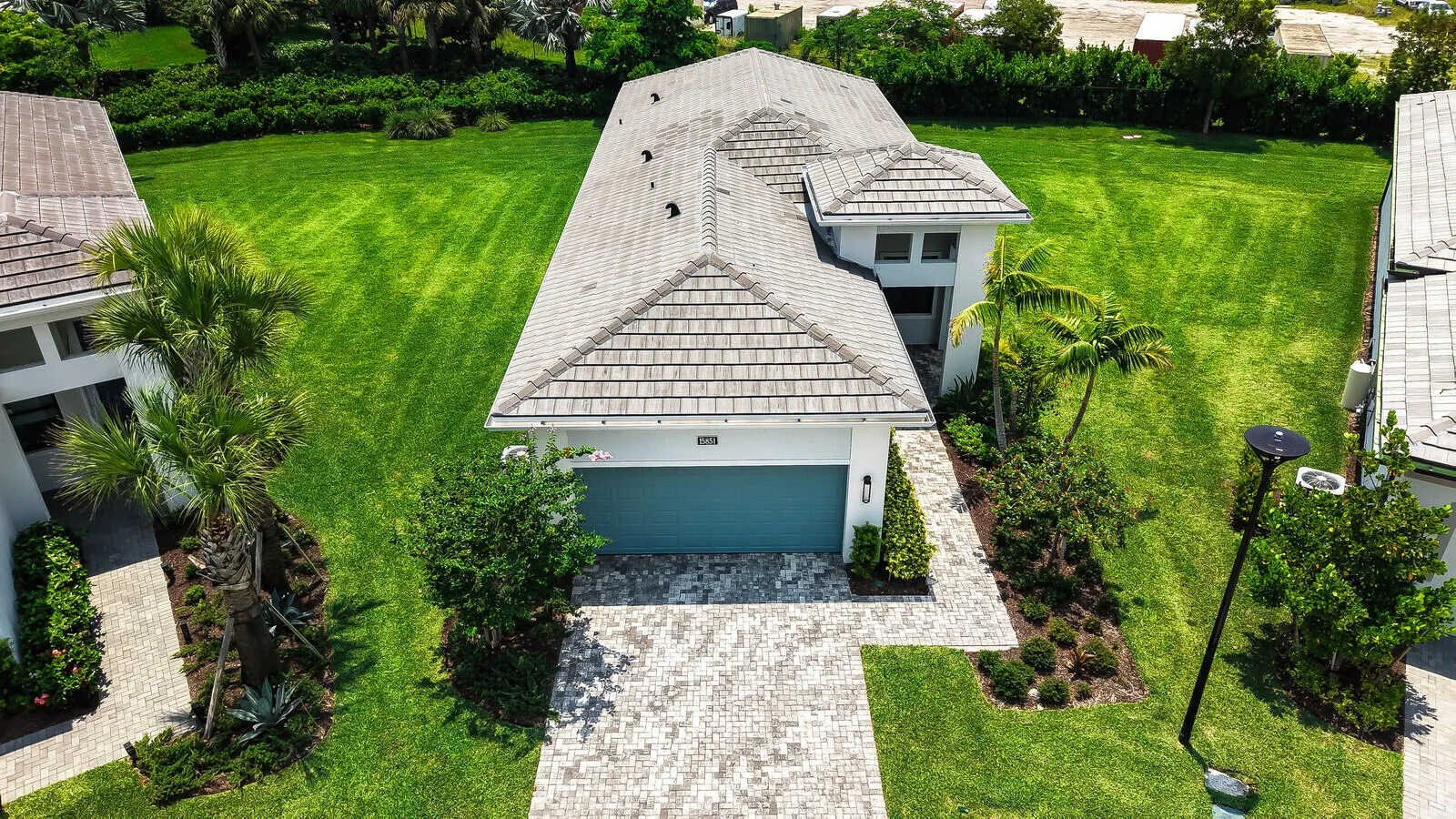 Contemporary residence featuring a light-toned tile roof, an integrated garage with a teal door, and a paver driveway