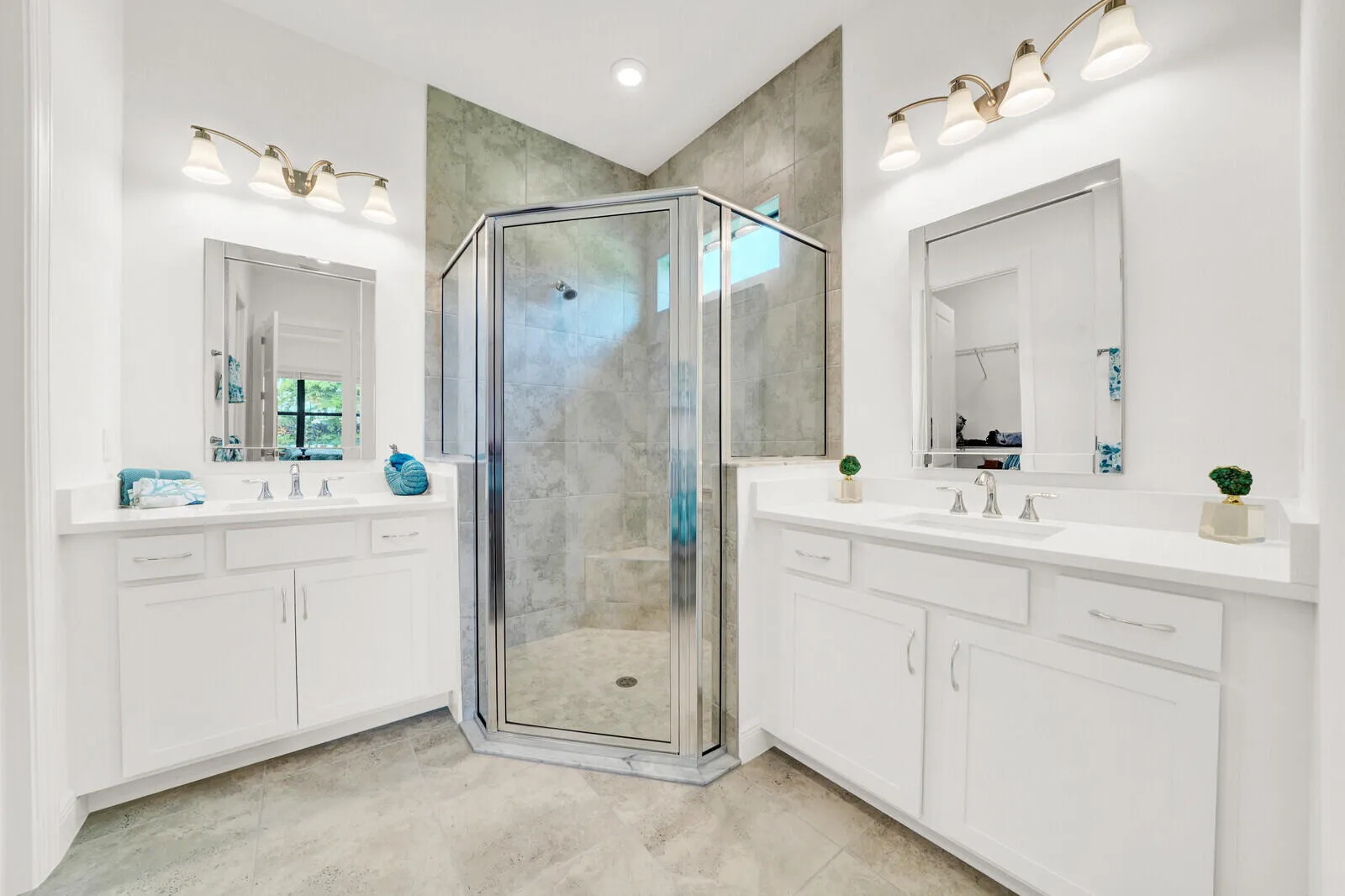 Spacious bathroom featuring a glass-enclosed shower with tile surround, dual vanity sinks, white cabinetry, polished chrome fixtures, and large format tile flooring