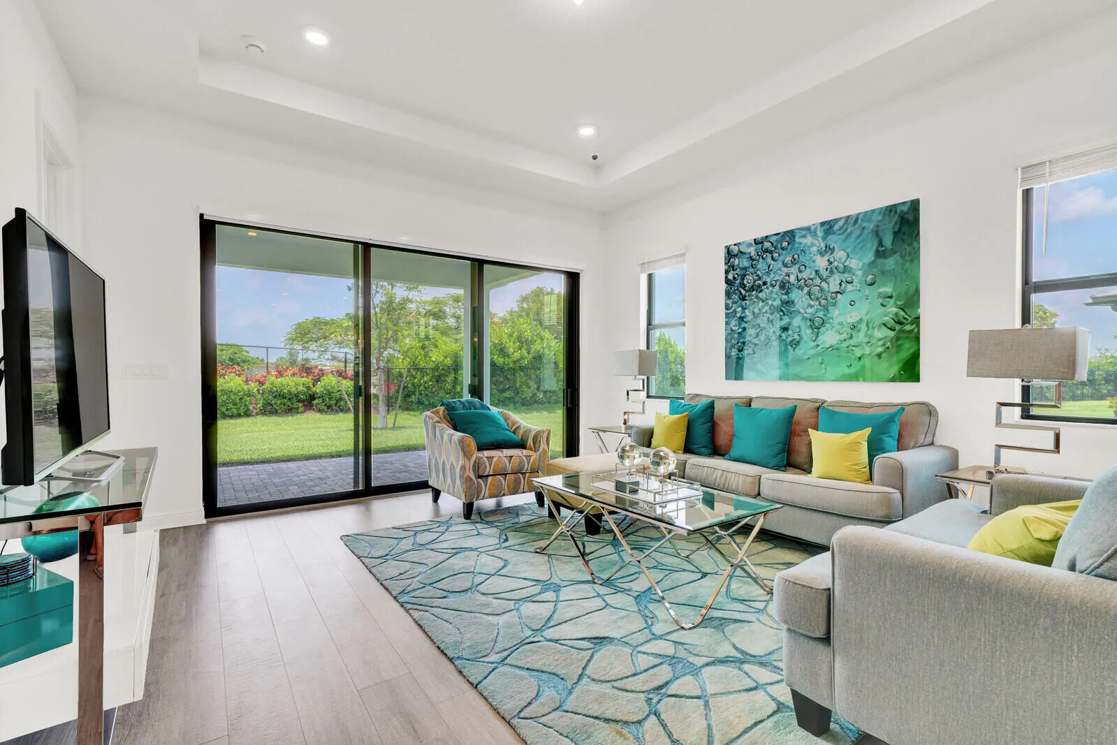 Spacious living area featuring wood-finish flooring, a tray ceiling with recessed lighting, and large sliding glass doors leading to outdoor patio space and a manicured lawn