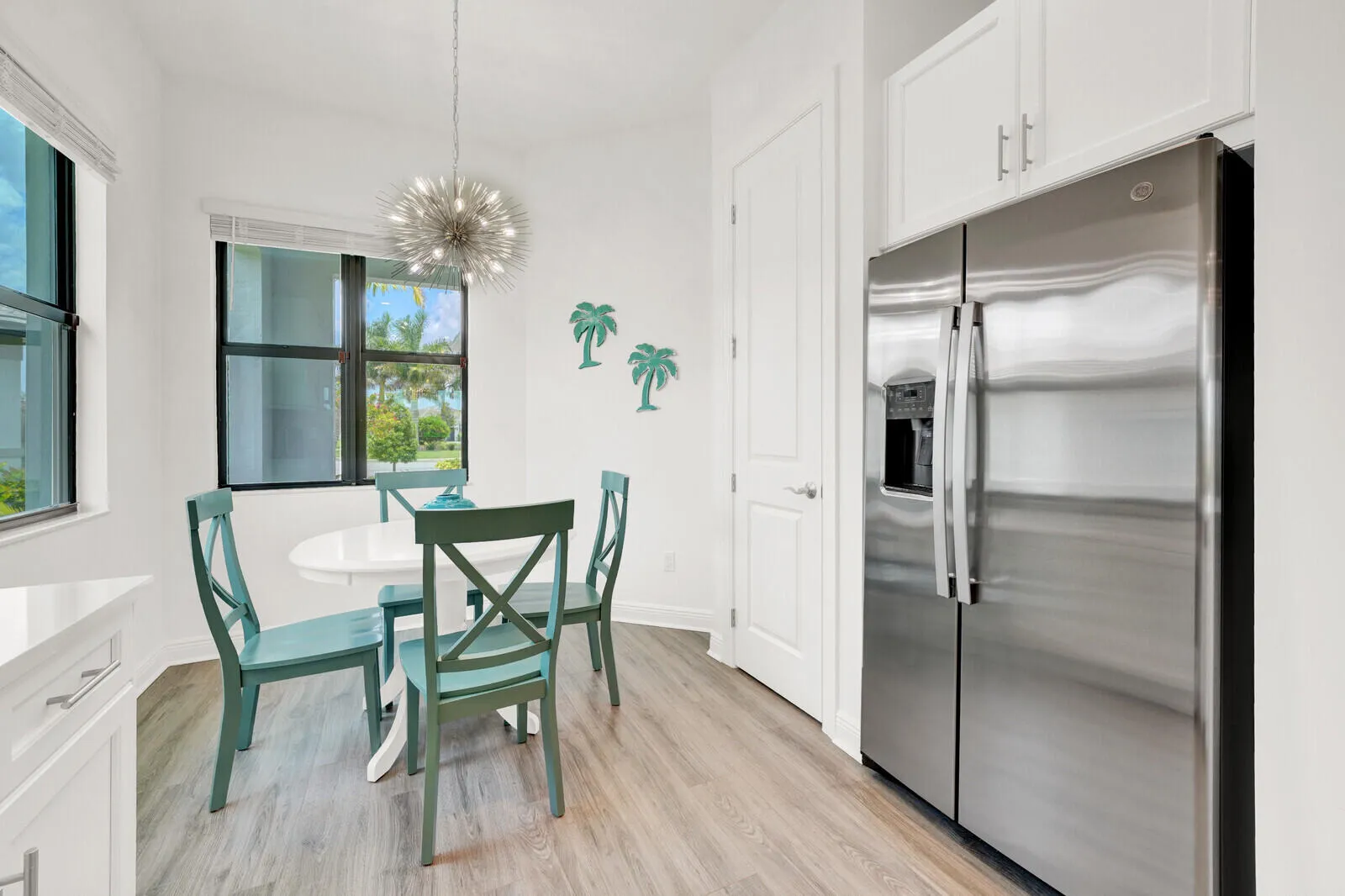 Contemporary dining nook featuring a modern sputnik-style chandelier, expansive windows, wood-finish flooring, and a stainless steel side-by-side refrigerator