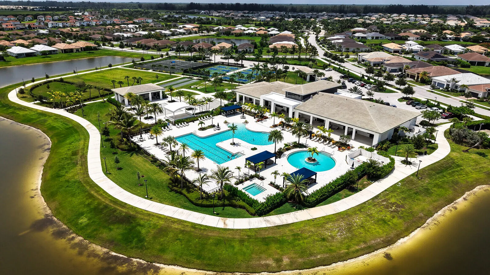 Community clubhouse featuring multiple swimming pools, sports courts, and manicured green spaces