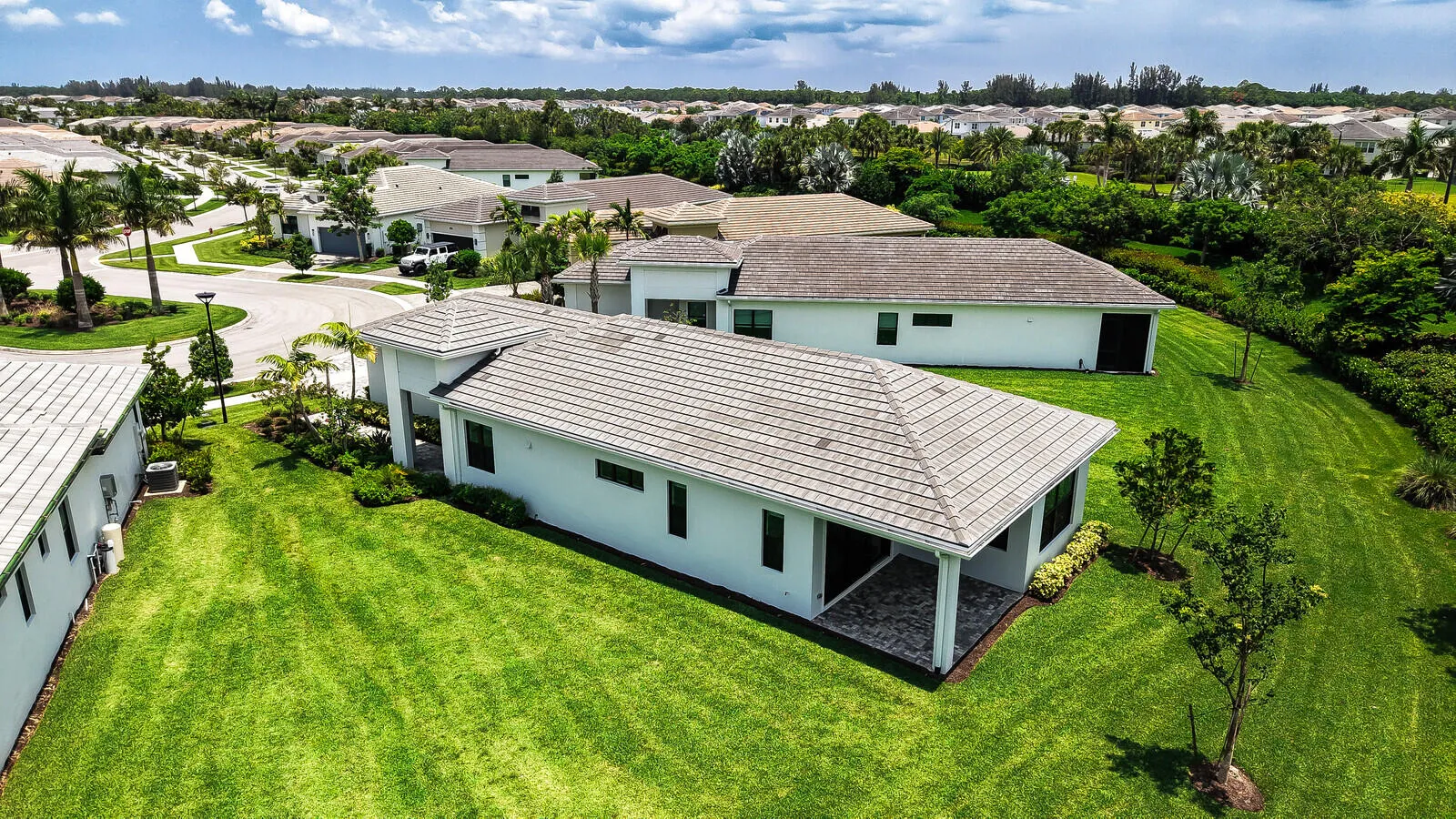 Contemporary white stucco residence featuring a gray tile roof, screened lanai with paver flooring, and extensive green lawn
