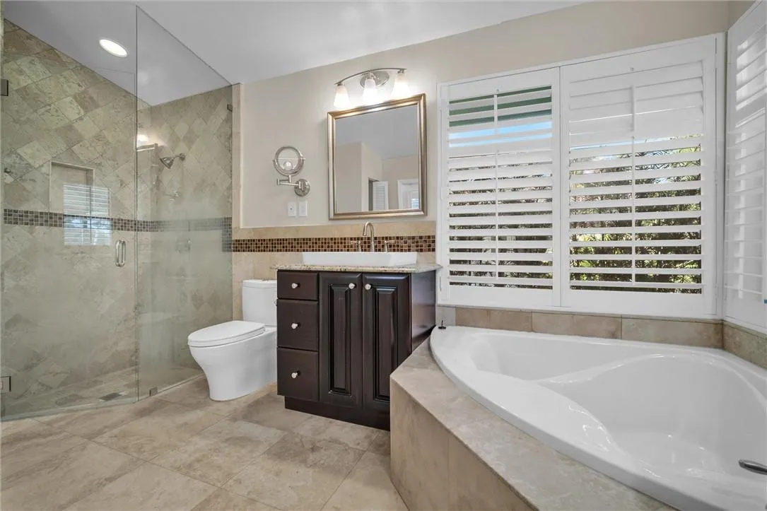 Remodeled master bathroom with double wood cabinetry vanities, seamless shower, oversized tub, plantation shutters, linen closet and access to pool area through cabana bath door.