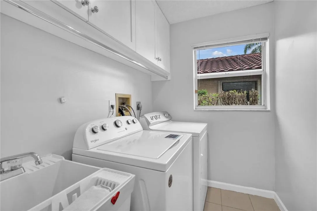 Light, bright laundry room with washer, dryer, sink & white cabinets.