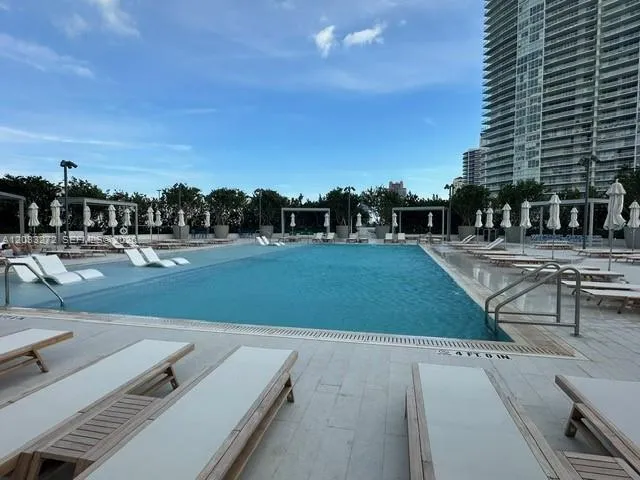 Swimming pool featuring a tiled deck, metallic handrails, perimeter lighting, and shaded structural cabanas