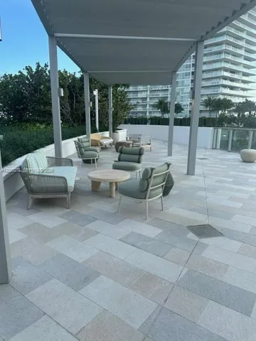Outdoor terrace featuring light-toned stone tile flooring, a metal pergola, low-profile perimeter walls, and built-in wall-mounted lighting