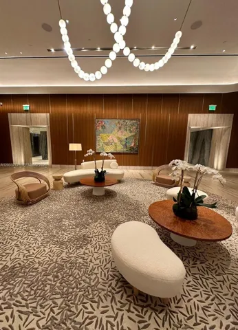 Lobby featuring vertical wood-paneled walls, stone-surround recessed entryways, patterned wall-to-wall carpeting, and a custom circular-link ceiling fixture