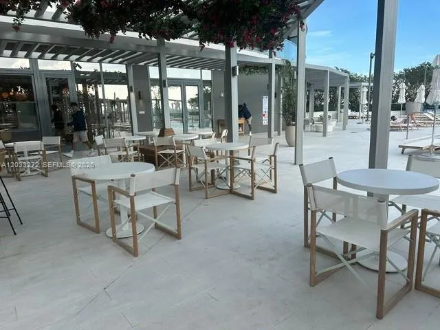 Expansive covered patio featuring light-toned tile flooring, structured metal framing, and extensive glass-paneled walls