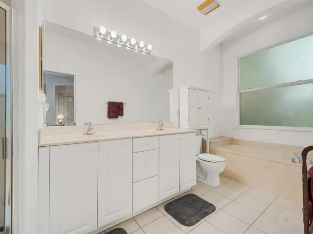 Bathroom featuring a double vanity with light-colored countertops, an integrated soaking tub, and a large frosted window