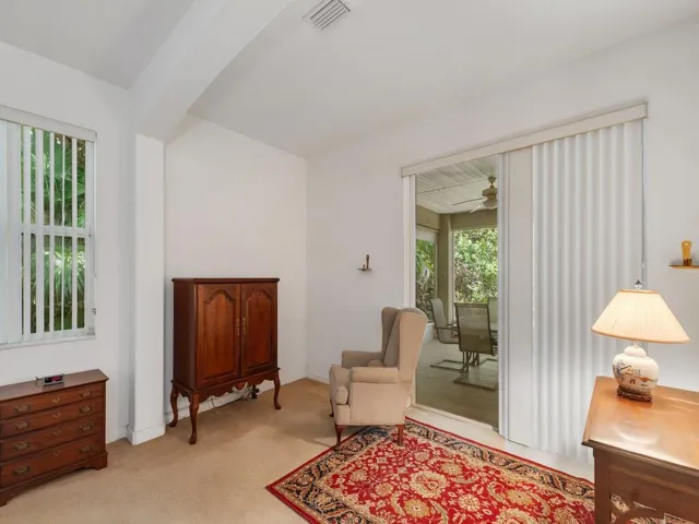 Carpeted room with a ceiling fan, a window with vertical blinds, and an open doorway leading to a bathroom with a white vanity and mirror