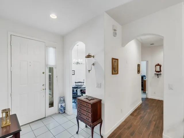 Entryway featuring a white paneled door with a sidelight, white square tile flooring, recessed lighting, and an arched doorway leading to a dining area with a chandelie