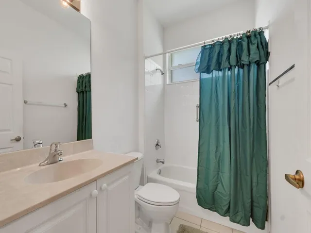 Bathroom featuring a vanity with an integrated sink and light-toned countertop, a full-sized mirror, a toilet, and a combination tub and shower with white tile surround