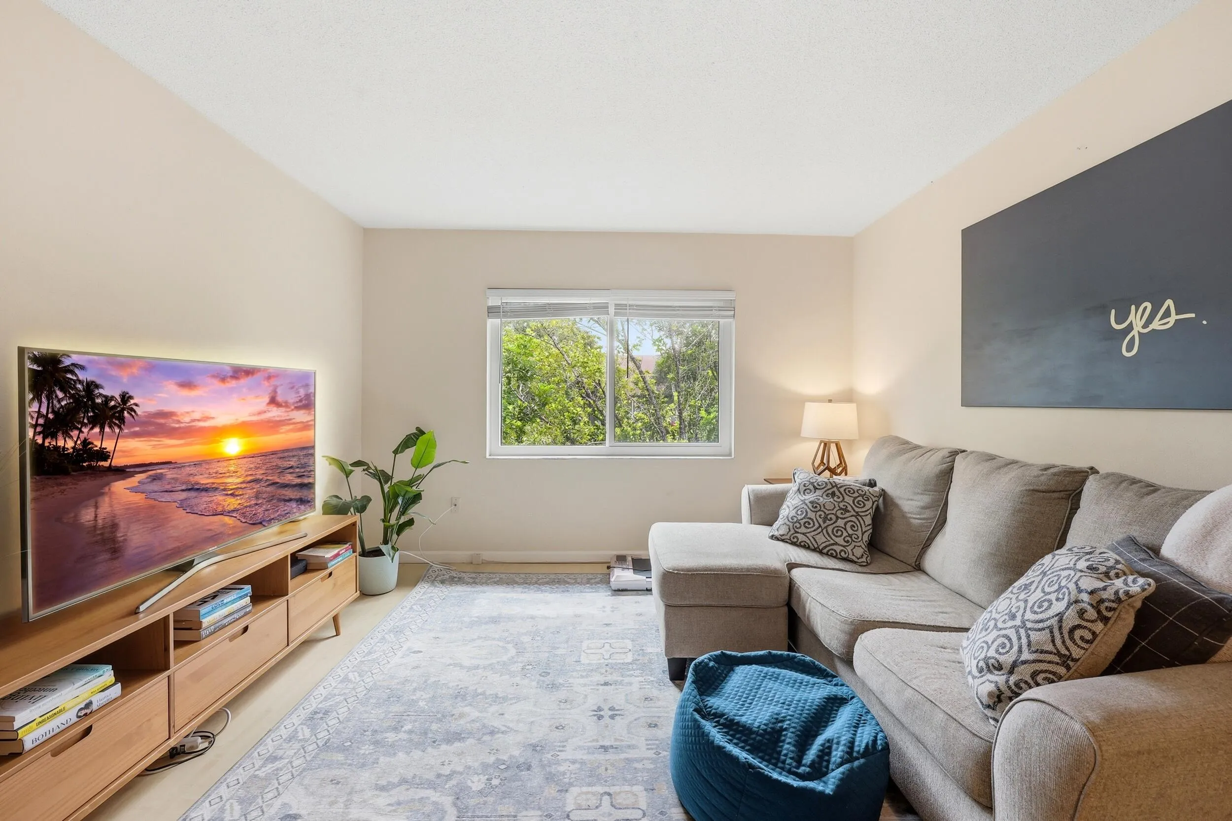 The spacious living room is filled with natural light and offers a comfortable setting for both relaxing and entertaining. Large windows frame peaceful treetop views, creating a bright and inviting atmosphere throughout the day. The open-concept layout flows seamlessly into the dining area, while neutral finishes and wood-look flooring provide a clean, versatile backdrop for any design style. Ample wall space and an efficient floor plan maximize both functionality and comfort, making this the perfect place to unwind or gather with friends and family.