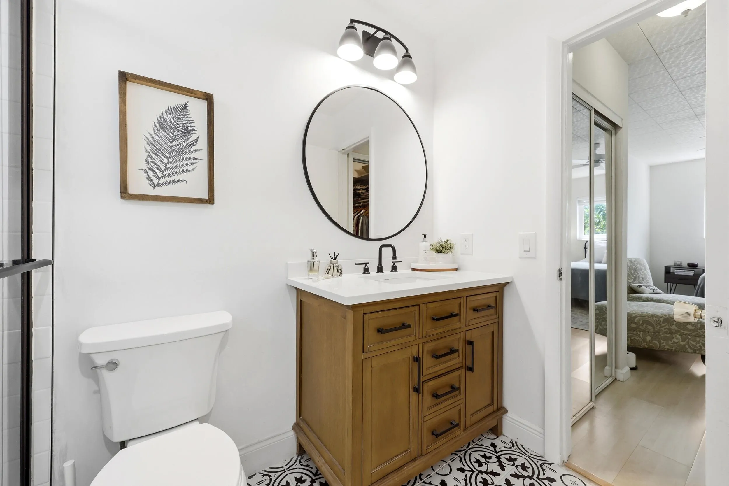 Beautifully renovated, the bathroom blends timeless design with modern functionality. The space features a custom vanity with abundant storage, a quartz countertop, matte black fixtures, designer tile flooring, and a striking round mirror that creates a clean, contemporary feel. The walk-in shower is finished with classic subway tile, a frameless glass enclosure, and a transom window that fills the room with natural light. Thoughtful finishes and quality craftsmanship make this bathroom feel more like a private spa retreat than a typical condominium bath.