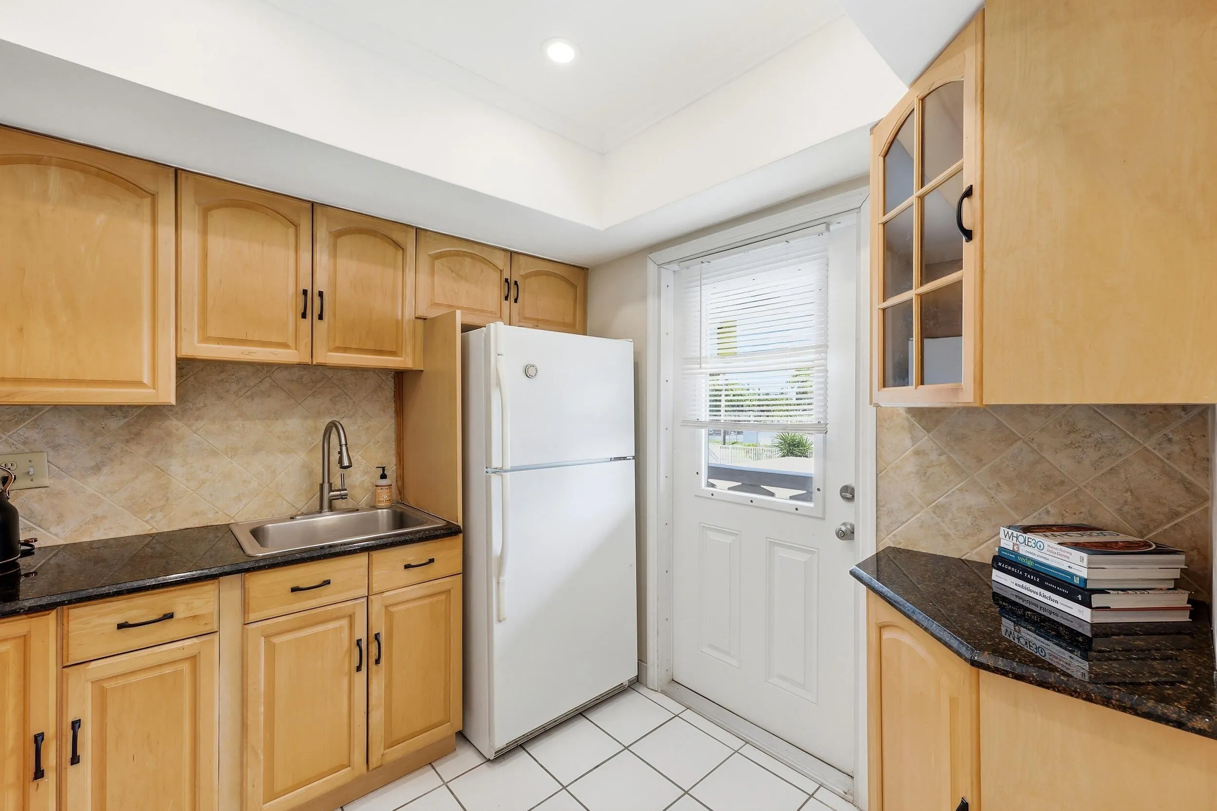 The kitchen offers an efficient and functional layout with abundant cabinet storage, granite countertops, and a neutral tile backsplash that complements the warm wood cabinetry. A tray ceiling enhances the sense of space while ample counter space makes meal preparation easy and convenient. Thoughtful details, including glass-front display cabinetry and additional storage options, provide both practicality and charm. The kitchen also features direct access to the private balcony, allowing natural light to filter in while creating a seamless connection between indoor and outdoor living. A new garbage disposal and new electrical panel were both installed in 2025, adding peace of mind for the next owner.