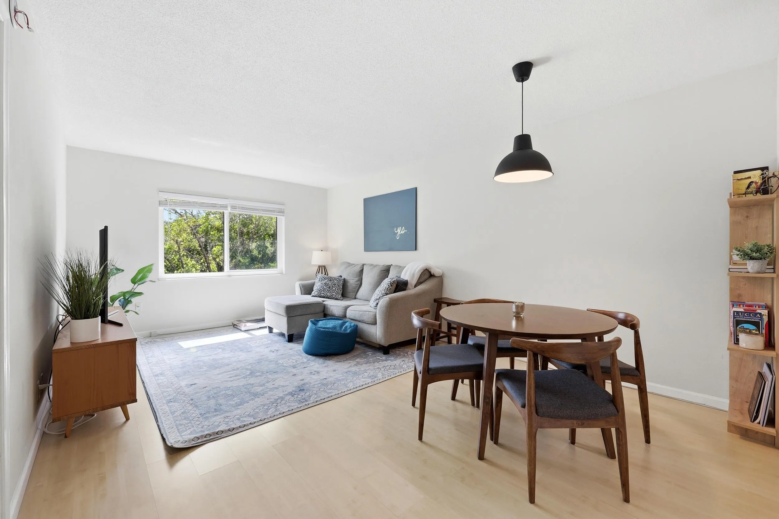 The spacious living room is filled with natural light and offers a comfortable setting for both relaxing and entertaining. Large windows frame peaceful treetop views, creating a bright and inviting atmosphere throughout the day. The open-concept layout flows seamlessly into the dining area, while neutral finishes and wood-look flooring provide a clean, versatile backdrop for any design style. Ample wall space and an efficient floor plan maximize both functionality and comfort, making this the perfect place to unwind or gather with friends and family.