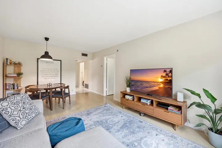 The spacious living room is filled with natural light and offers a comfortable setting for both relaxing and entertaining. Large windows frame peaceful treetop views, creating a bright and inviting atmosphere throughout the day. The open-concept layout flows seamlessly into the dining area, while neutral finishes and wood-look flooring provide a clean, versatile backdrop for any design style. Ample wall space and an efficient floor plan maximize both functionality and comfort, making this the perfect place to unwind or gather with friends and family.
