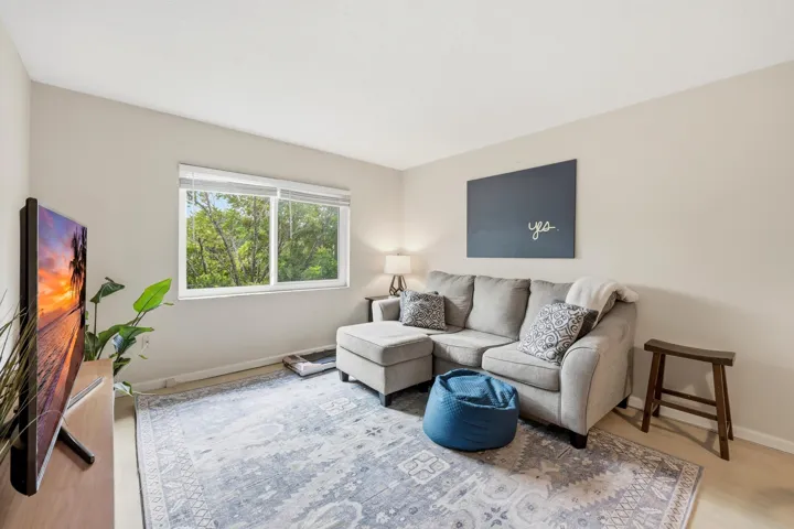 The spacious living room is filled with natural light and offers a comfortable setting for both relaxing and entertaining. Large windows frame peaceful treetop views, creating a bright and inviting atmosphere throughout the day. The open-concept layout flows seamlessly into the dining area, while neutral finishes and wood-look flooring provide a clean, versatile backdrop for any design style. Ample wall space and an efficient floor plan maximize both functionality and comfort, making this the perfect place to unwind or gather with friends and family.