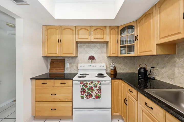 The kitchen offers an efficient and functional layout with abundant cabinet storage, granite countertops, and a neutral tile backsplash that complements the warm wood cabinetry. A tray ceiling enhances the sense of space while ample counter space makes meal preparation easy and convenient. Thoughtful details, including glass-front display cabinetry and additional storage options, provide both practicality and charm. The kitchen also features direct access to the private balcony, allowing natural light to filter in while creating a seamless connection between indoor and outdoor living. A new garbage disposal and new electrical panel were both installed in 2025, adding peace of mind for the next owner.