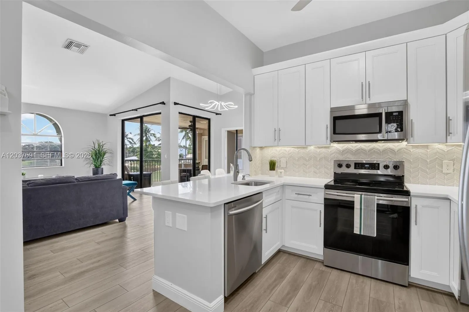 Remodeled kitchen with quartz counters, stainless appliances, under-cabinet lighting and custom herringbone tile backsplash