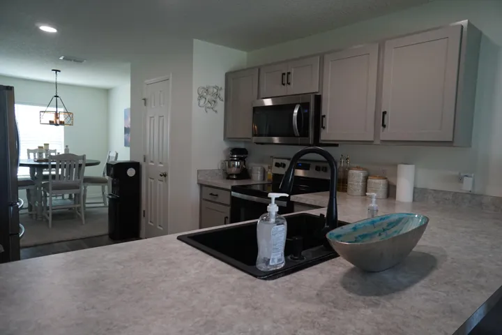 Kitchen featuring light grey cabinetry with black hardware, stainless steel appliances, and a black sink with a gooseneck faucet