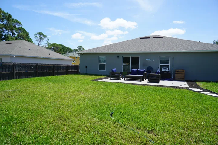Expansive backyard featuring a lush lawn, privacy fencing, and a concrete patio