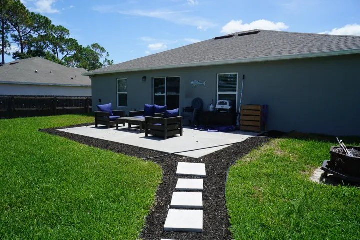 Expansive backyard featuring a concrete patio, stepping stone pathway, and a perimeter of dark mulch