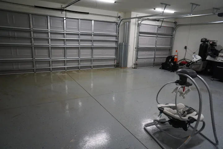 Spacious garage featuring two sectional doors, overhead lighting, and a durable epoxy-coated floor. Pull-down stairs for easy access to attic