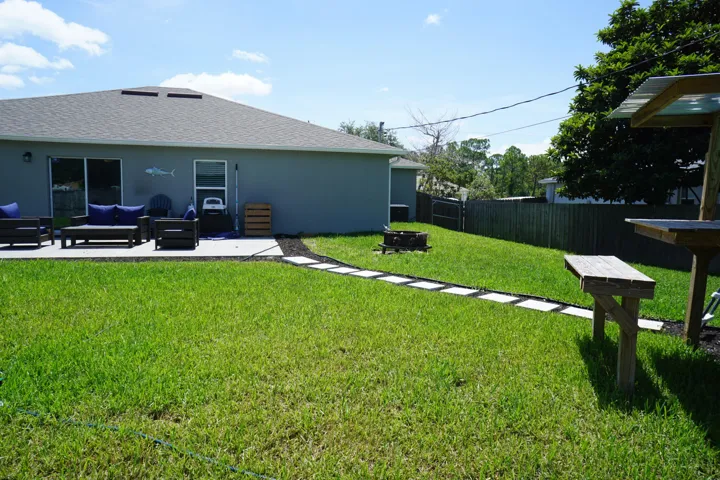 Expansive grassy backyard featuring a concrete patio, sliding glass door, and a stepping stone pathway