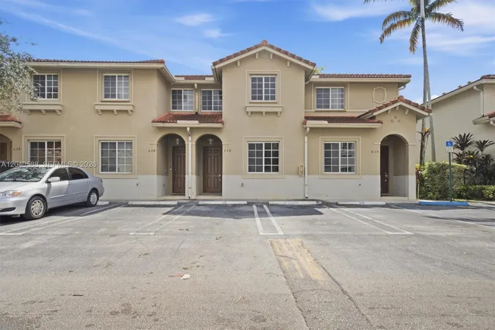Stucco exterior with a tiled roof, multi-pane windows, arched entryways, and designated parking spaces