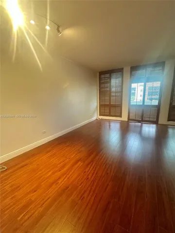 Spacious room showcasing rich wood-finish flooring, white painted walls, recessed lighting, and glass sliding doors with louvered panels providing natural light and access to outdoor space