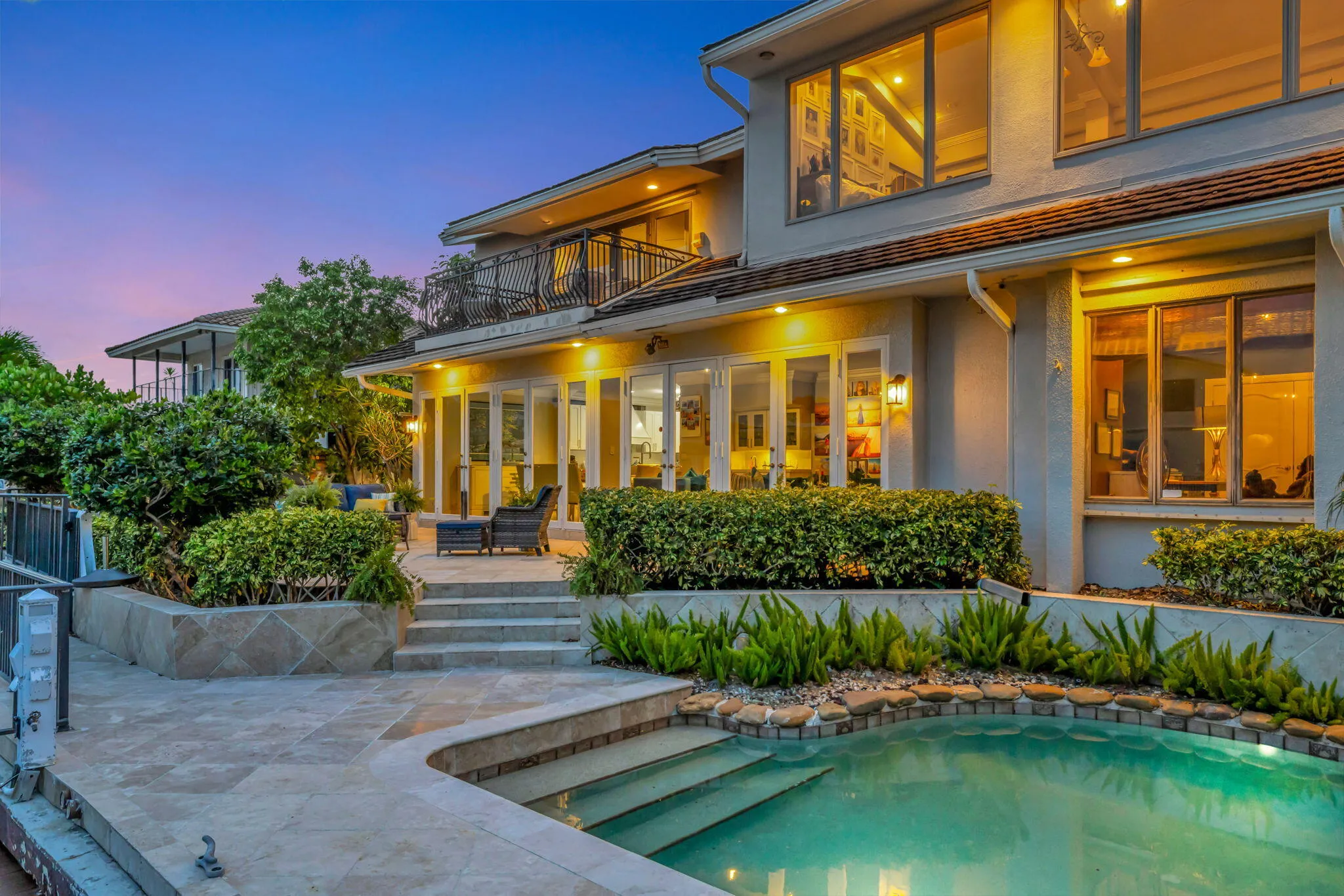 The illuminated rear elevation, pool, and waterfront setting create a strong evening hero image.