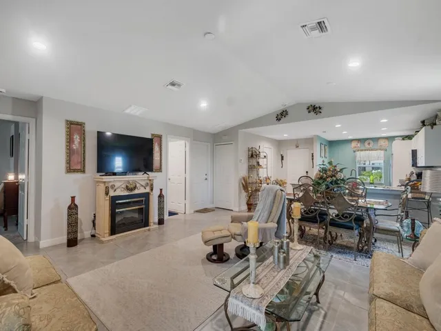 Open-concept living space featuring a decorative fireplace surround, tiled flooring, vaulted ceiling, recessed lighting, and a defined dining area
